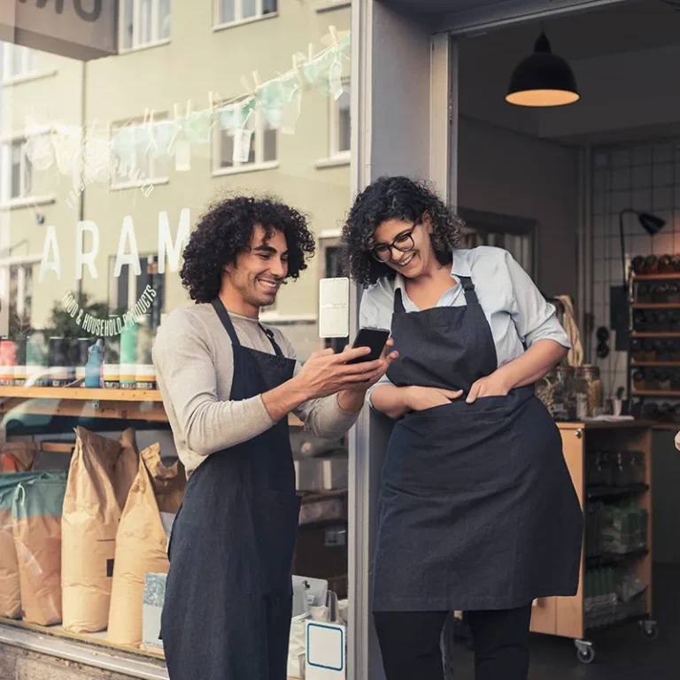 Dos emprendedores frente a una tienda usando el celular, imagen del programa Referidos Pyme Santander.